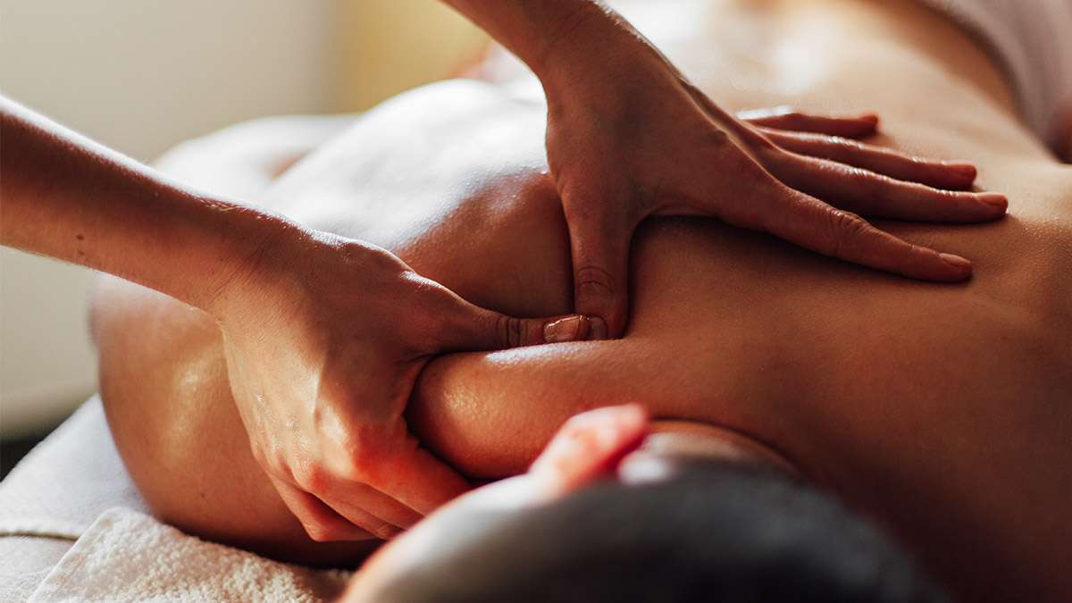 A close up view of a massage therapist uses her hands to massage the back of a patient.