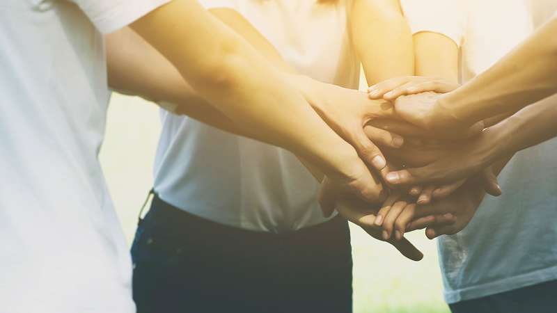 Several people stand huddled together in a circle as a team with all of their hands together