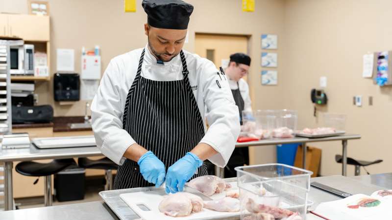 A whole chicken is cut and divided into clean pieces by a student.