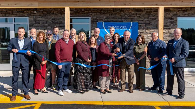 A large group of smiling people participates in a ribbon-cutting ceremony.