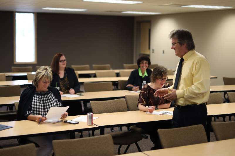 A businessman running a customized training session with several other professionals in attendance, seated at desks.