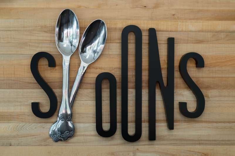 The sign for the Spoons Restaurant, mounted on wood paneling.