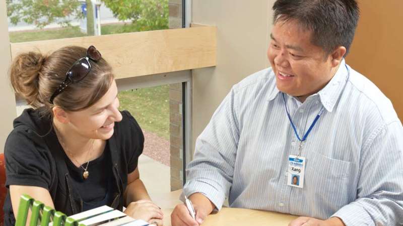 A student services employee is helping a student with paperwork at a desk inside of an office