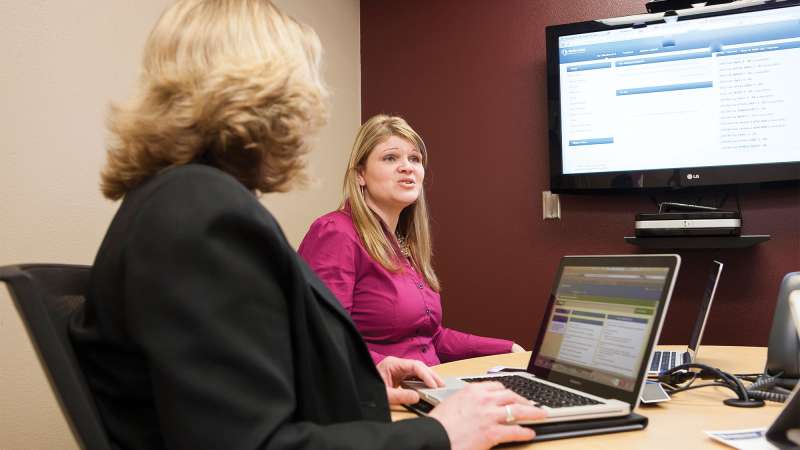 Two financial advisors sit next to each other in an office going over finanical information displayed on an overhead monitor