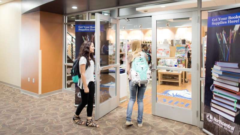 Two female students chat as they open the door to the campus store, before heading inside.