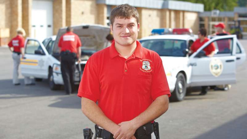 An NTC Security team member stands with his hands crossed in front of two squad cars