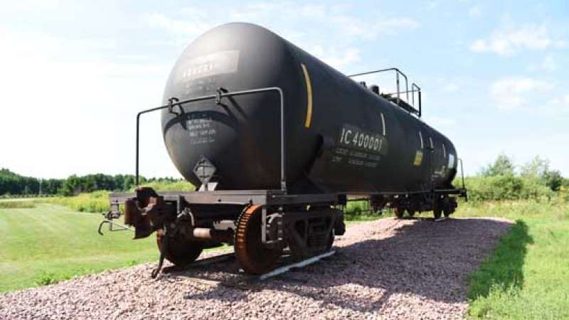 An oil tanker railcar sits in a gravel area.