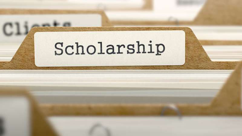 Several file folders are lined up with an emphasis on the word Scholarship labeled on a tab