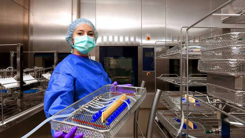 A young woman working in a hospital as a sterile processing technician. She is dressed in special medical hygiene clothing and carries out hygiene disinfecting and logistic tasks.