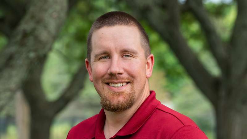 Adam Schneider smiling while standing in the courtyard on the Wausau Campus