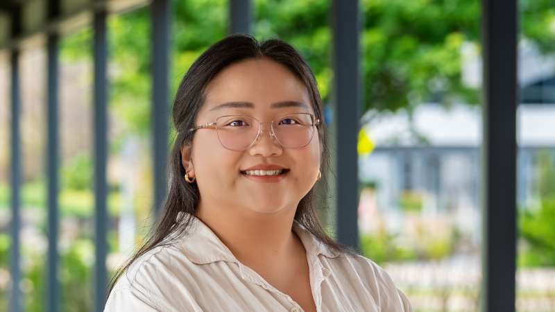 Pachia Moua smiling while standing under the covered walkway in front of the Wausau Campus