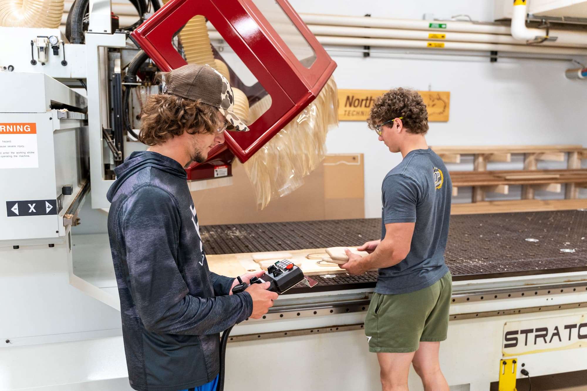 Two students examine the resulting products after running materials through a CNC router.