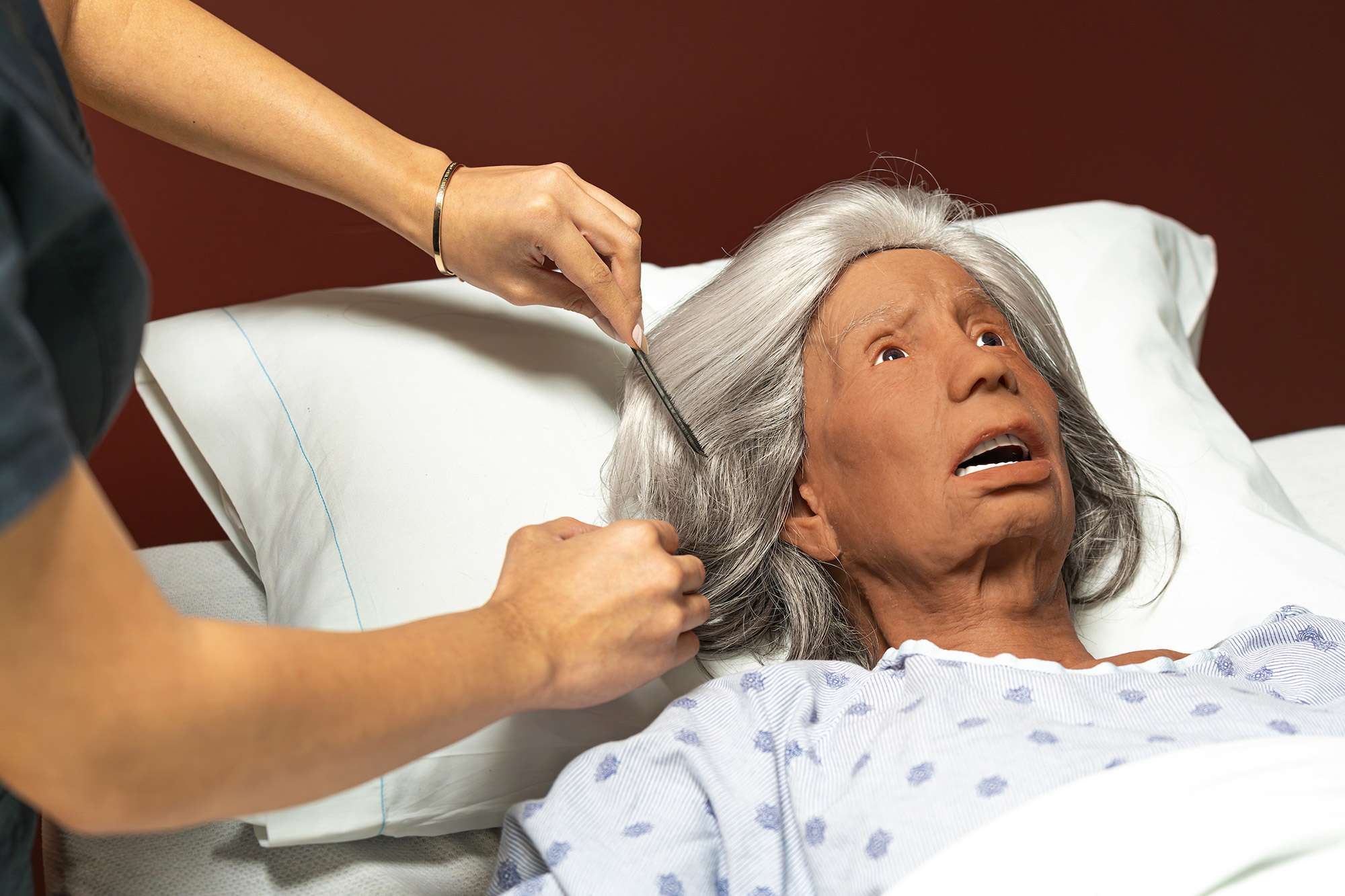 A Certified Nursing Assistant is combing the hair of a mannequin laying in a hospital bed.
