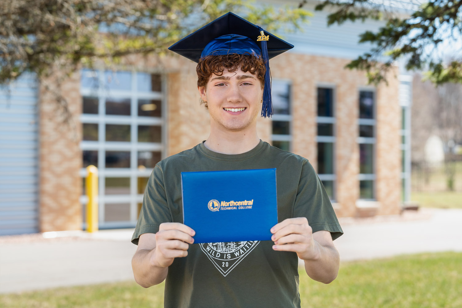 Aiden posing while wearing an NTC graduation cap and holding his diploma.