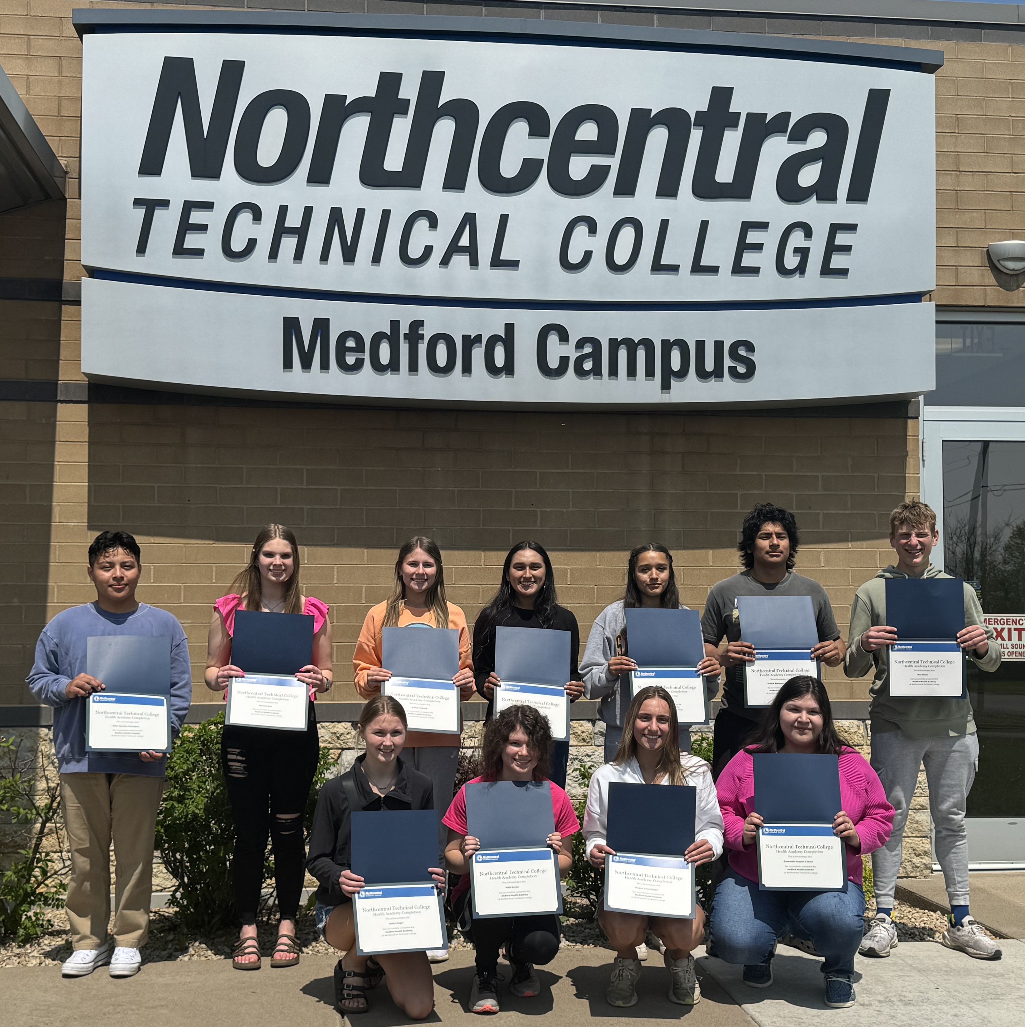 Medford Health Academy students posing outside in front of the NTC Medford Campus building, showing off their completion certificates.
