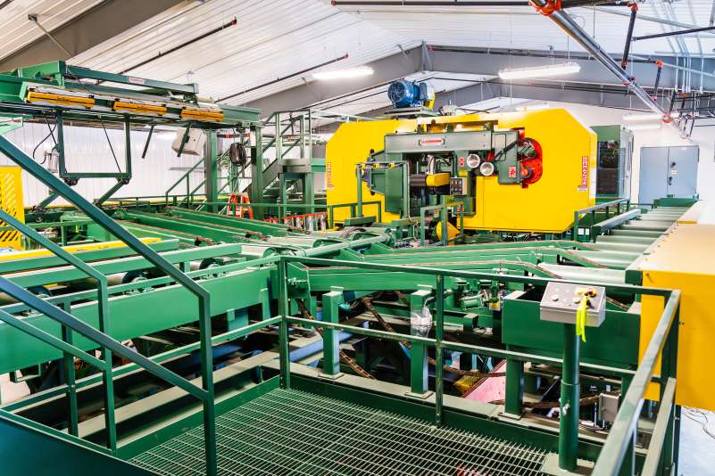 Wide-angle view of Northcentral Technical College’s sawmill facility, showcasing a large yellow Cleereman bandsaw, green conveyors, and integrated log scanning and control systems.